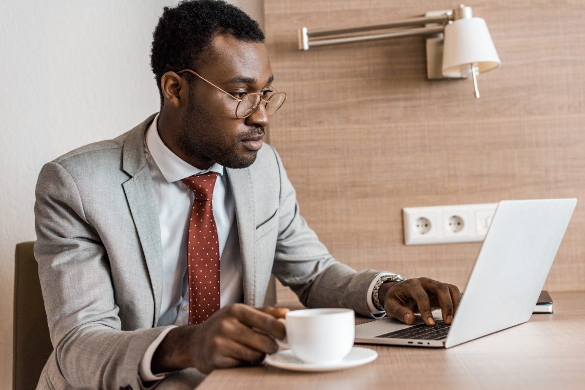 african american businessman with coffee working on laptop in hotel room