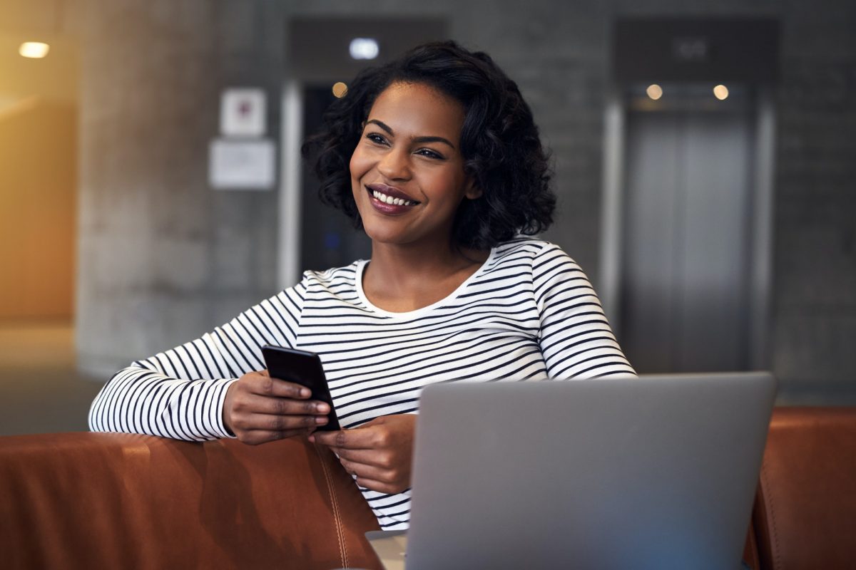 Smiling African student sending texts while studying between classes